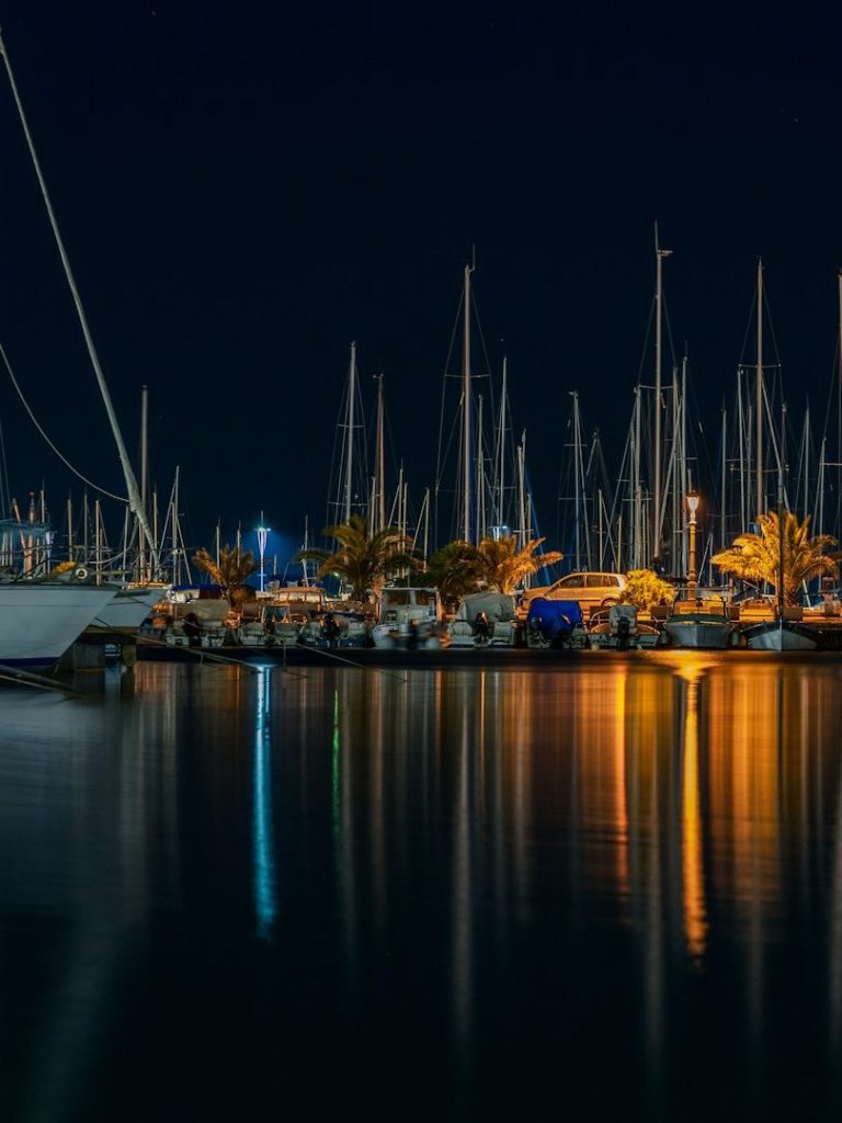 Hafen bei Nacht mit beleuchteten Booten und reflektierenden Lichtspielen im Wasser.