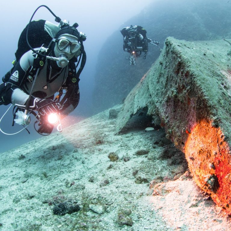 Ein Taucher betrachtet im Licht seines Unterwasserscheinwerfers ein Schiffywrack